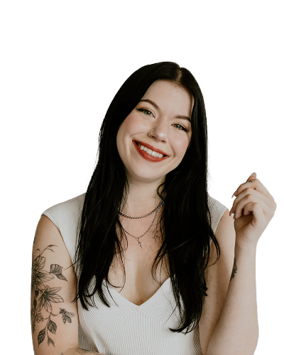 A woman with long black hair, wearing a white sleeveless top and layered necklaces, smiles at the camera. She has floral tattoos on her left arm.