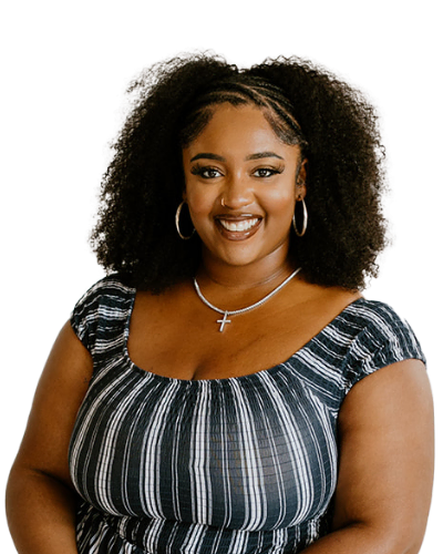 Woman with curly hair, wearing a striped top, hoop earrings, and a cross necklace, smiling at the camera against a plain white background.
