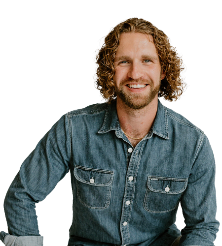 A man with curly hair and a beard is smiling, wearing a denim shirt, and seated against a plain white background—perfect for showcasing personality in your Teams section.