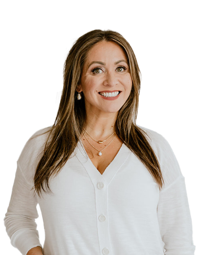 Woman with long brown hair wearing a white sweater and layered necklaces, smiling at the camera against a plain white background.