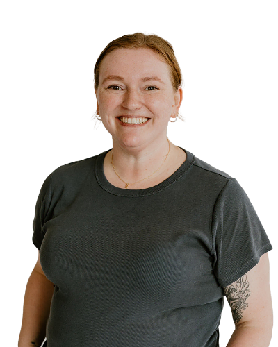 A person with reddish-brown hair in a ponytail, wearing a dark gray t-shirt, smiles at the camera against a plain white background.