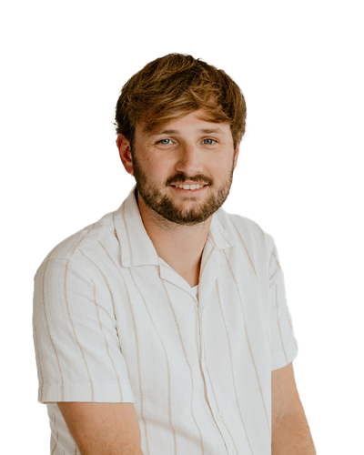 A man with short brown hair and a beard is wearing a white, short-sleeved, button-up shirt with thin stripes, seated against a plain white background.