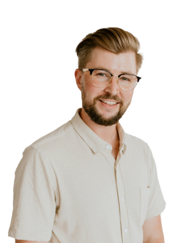 A man with light brown hair, glasses, and a beard is wearing a light-colored short-sleeve shirt and smiling at the camera against a plain white background.