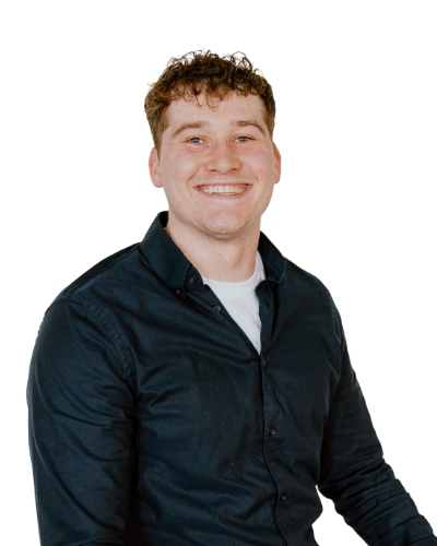 A young man with curly hair wearing a dark button-up shirt over a white T-shirt is smiling at the camera against a plain white background.