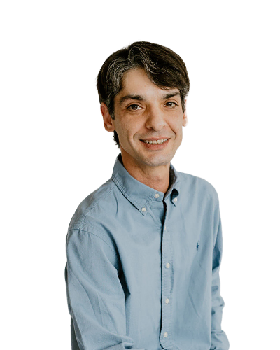 Man with short dark hair wearing a light blue button-up shirt, smiling, posed against a plain white background.