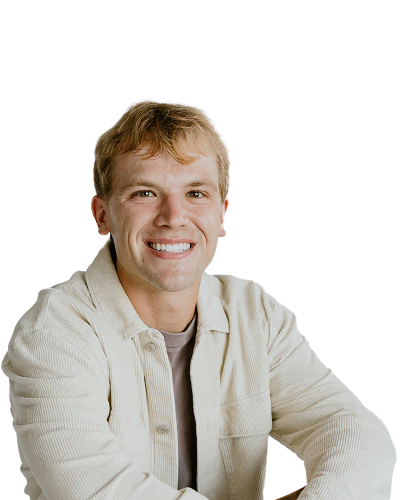 A young man with light hair, wearing a beige jacket over a gray shirt, smiles at the camera against a plain white background.