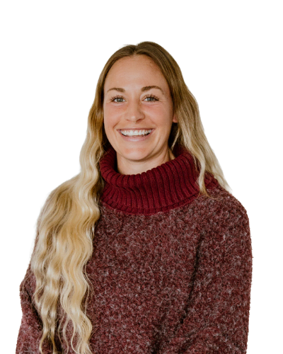 Woman with long wavy blonde hair wearing a maroon turtleneck sweater, smiling at the camera against a plain white background.