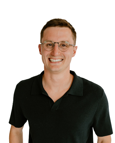 A man wearing glasses and a black collared shirt smiles while standing against a plain white background.