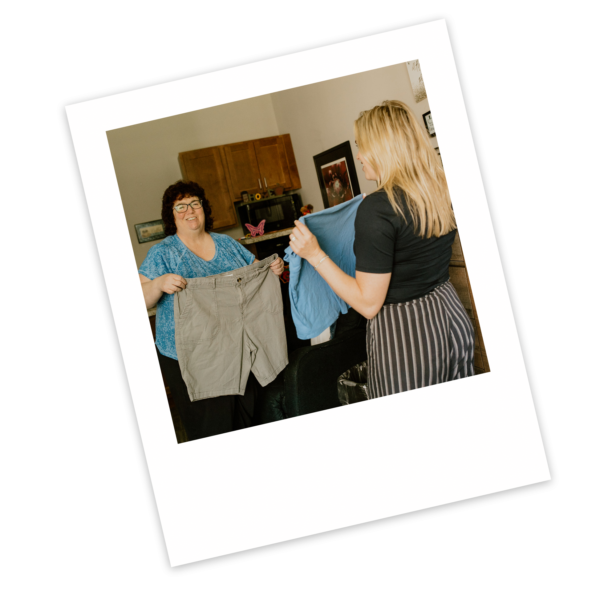Two women stand indoors, one holding a pair of shorts and the other a blue shirt, appearing to sort or discuss clothing as part of an ECCG initiative.