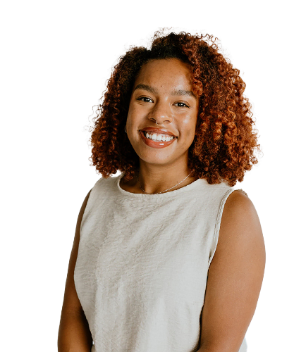 A woman with curly, shoulder-length hair smiles at the camera while wearing a sleeveless light-colored top against a plain white background.