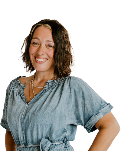 Woman with wavy brown hair wearing a blue short-sleeve blouse stands against a plain white background, smiling at the camera.